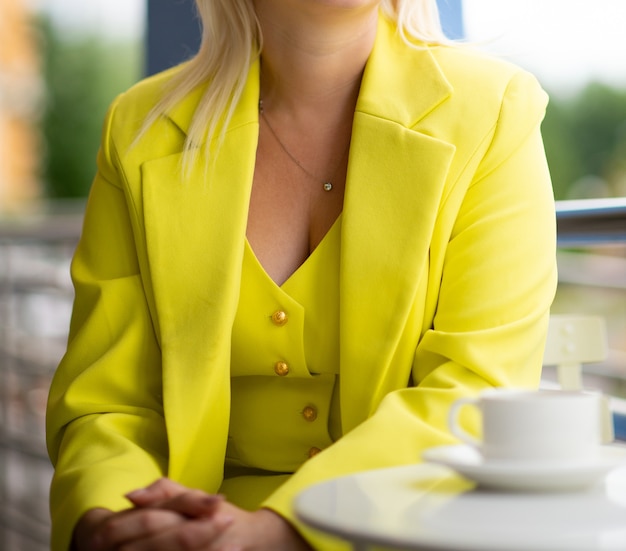 Woman in a bright yellow business suit at a table in a summer cafe, unrecognizable