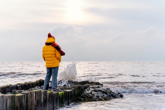 Woman in bright yellow jacket walking alone on  seaside on cold winter day Travel Lifestyle concept