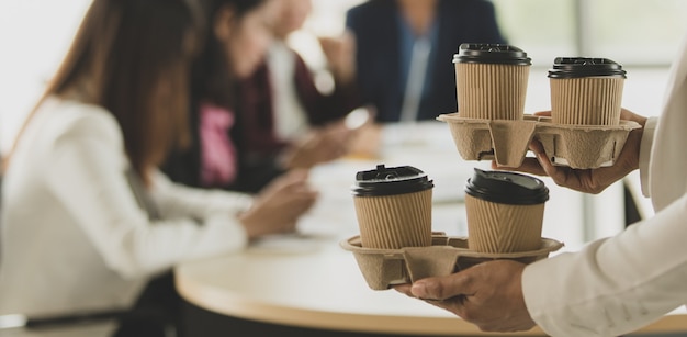 Foto la donna porta i bicchieri di caffè da asporto in ufficio durante un gruppo di dipendenti, colleghi seduti e lavorano alla scrivania e poi salutano e felici con gentilezza. concetto di lavoro di squadra.