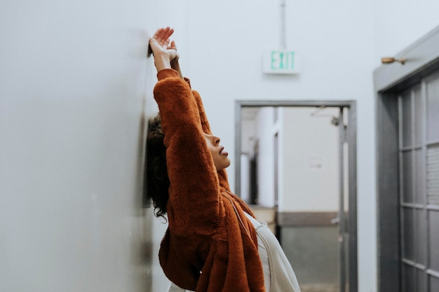 Woman in a brown coat leaning against a wall