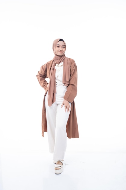 A woman in a brown coat and white pants stands in front of a white background