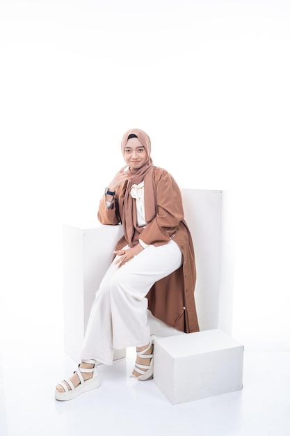 A woman in a brown outfit sits on a white chair with a black watch on her left hand.