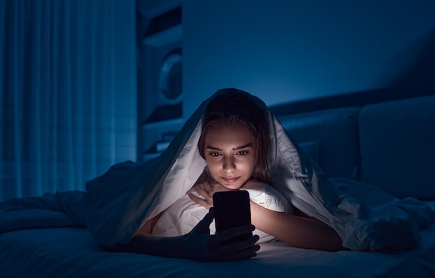 Woman browsing smartphone in bed at night