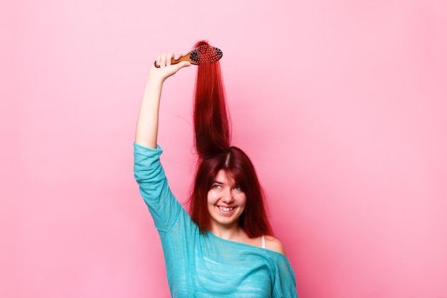 Woman brushing her hair on pink background