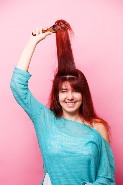 Woman brushing her hair on pink background