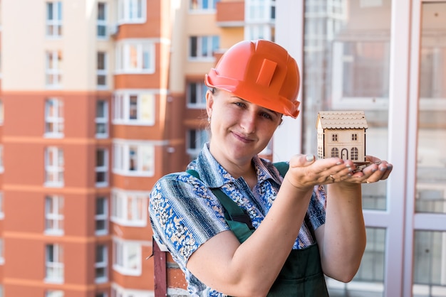 Woman in builder helmet holding house model and keys