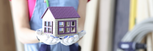 Woman builder holding toy wooden house in hands closeup