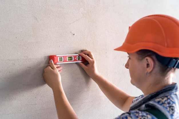 Woman builder measuring wall by water level instrument