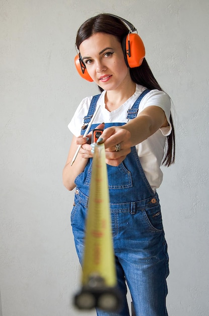 Woman builder in protective gloves, construction clothes holds a tape measure in her hands.