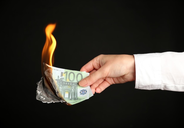 Woman burning Euros banknotes on black background