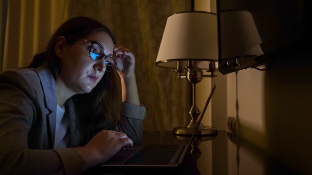 Photo woman in a business suit in a dark evening sits at a laptop, slow motion