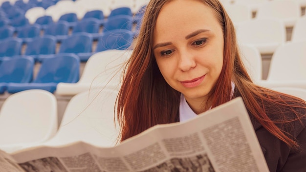 A woman in a business suit reads a newspaper while sitting at the stadium