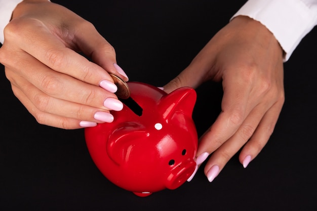 Woman businessman puts coin in piggy bank on black background