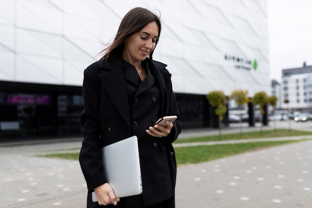 Woman businessman with a laptop in his hands looks at a mobile phone on the background of an office