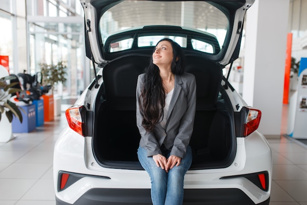 Donna che acquista auto nuove in showroom, signora vicino al bagagliaio aperto.