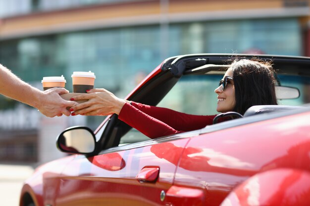 Photo woman in cabriolet picks up hot drinks from a courier. food and drink delivery concept