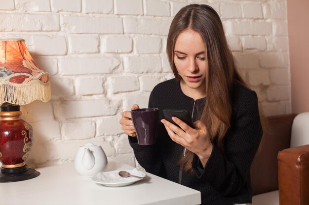 Donna in caffè che beve tè e usa il suo smartphone