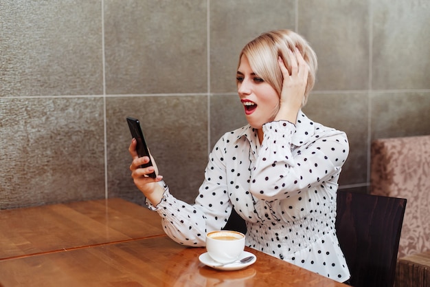 Woman in cafe looking at smartphone and wondering