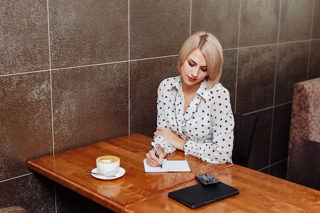 Woman in cafe sitting and writing in notebook