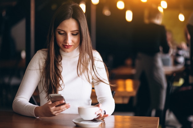 電話とコーヒーを持つカフェの女性