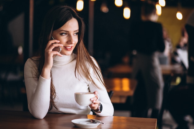 電話とコーヒーを持つカフェの女性