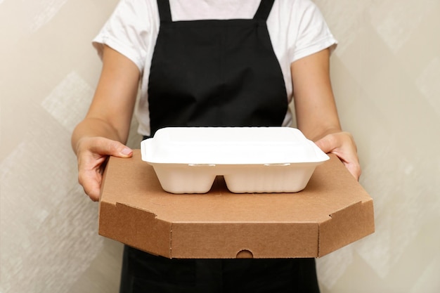 a woman cafe worker serves a completed takeaway order boxed pizza and a container with food in disposable utensils made from recycled raw materials