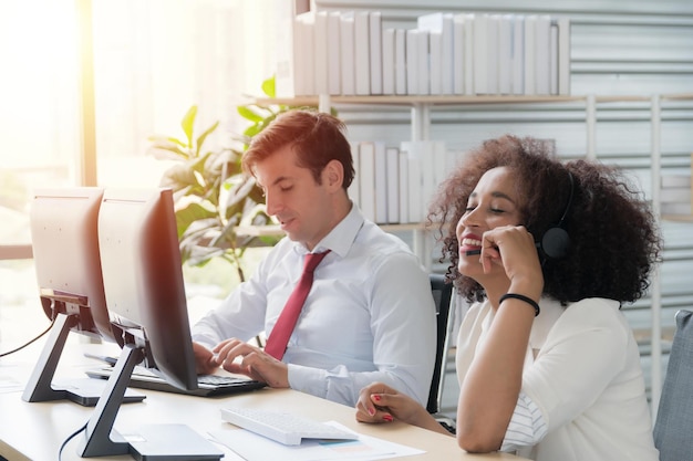 Woman call center African American wearing white work clothes with headset working in call center at computer