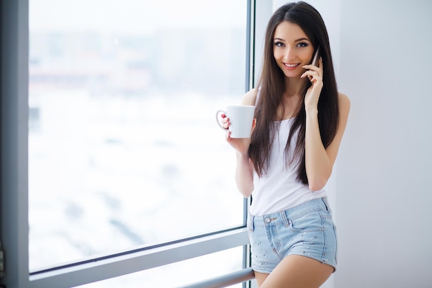 Photo woman calling on smartphone at window in morning