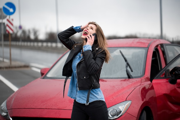 Woman calls to a service standing by a red car