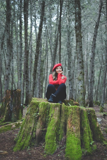 Woman in a calm and thoughtful attitude on a mossy stump in the middle of the forest