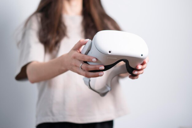 A woman captured from the chest up holds a white pair of virtual reality glasses with both hands