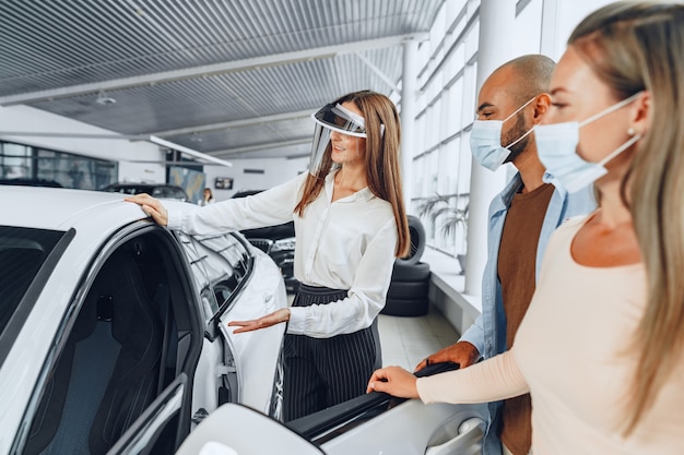 Woman car dealer consulting buyers wearing medical face shield