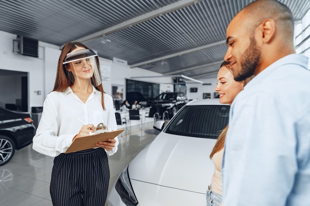 Woman car dealer consulting buyers wearing medical face shield