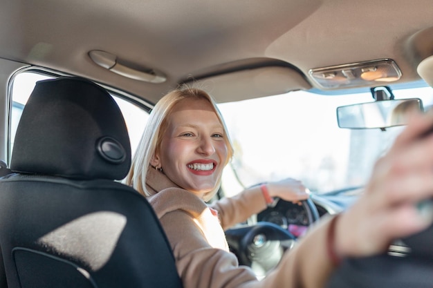 Woman in car indoor turning around looking at passengers in back seat idea taxi driver Concept of exam Vehicle Back view of an attractive young woman looking over her shoulder while driving a car