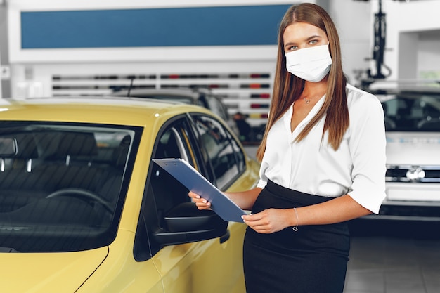 Foto venditore di auto donna in piedi vicino a un'auto nuova che indossa la maschera protettiva