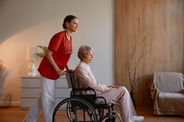 Woman caregiver preparing elderly lady in wheelchair for walk