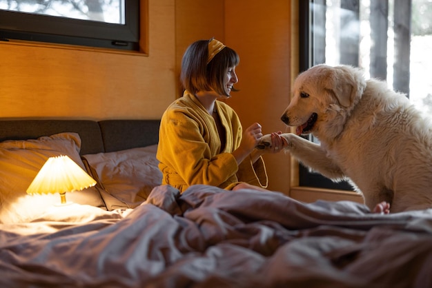 女性は自然の木の小屋の小さな寝室でベッドに横たわっている間、彼女の犬を気遣います