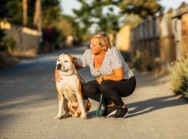 未舗装の通りに座っている犬を愛撫する女性