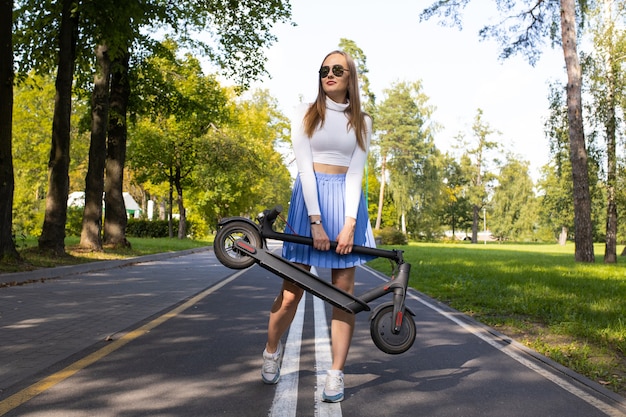 Woman carries her folded electric scooter in the park