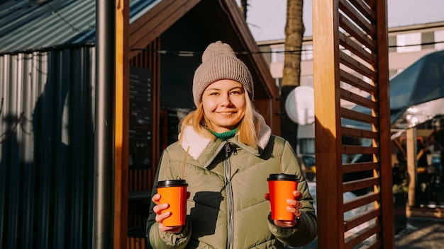 Woman carries two cups of coffee or mulled wine at the city outside food court