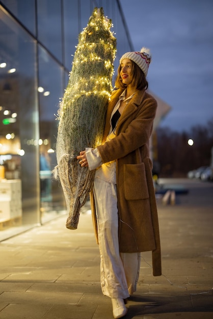 Женщина несет освещенную елку возле торгового центра