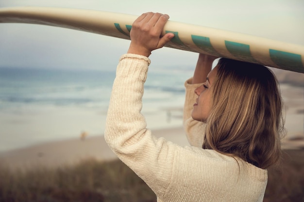 Foto donna che porta una tavola da surf sulla testa sulla spiaggia