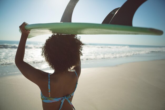 Photo woman carrying surfboard on her head at beach