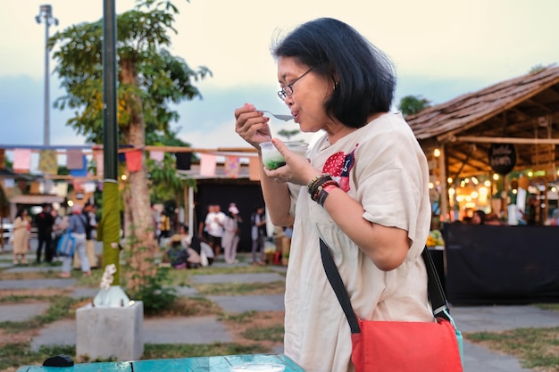 Woman in casual clothes standing and sipping Dawet a traditional Indonesian drink at a night market Solo Indonesia 20 June 2023