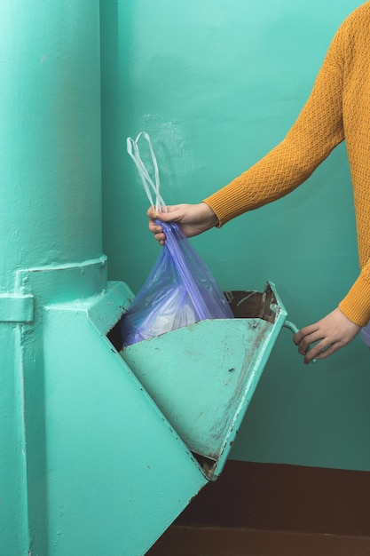 A woman in casual clothes throws a bag of garbage into the garbage chute. Close up