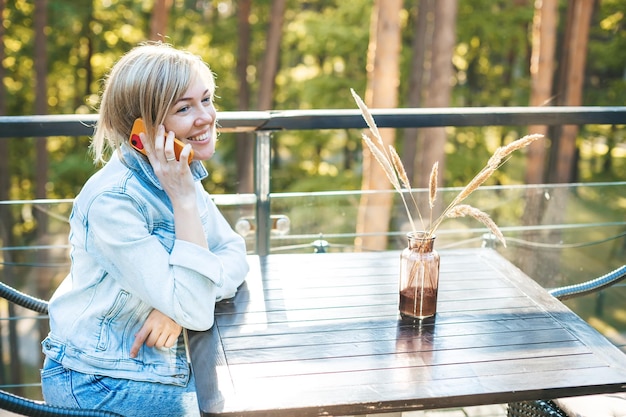 Woman in casual denim clothes talking on the phone sitting at the table outdoors