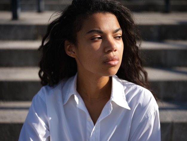 Foto donna in camicia bianca casual che sembra premurosa da parte mentre posa all'aperto in una calda giornata di sole. messa a fuoco selettiva