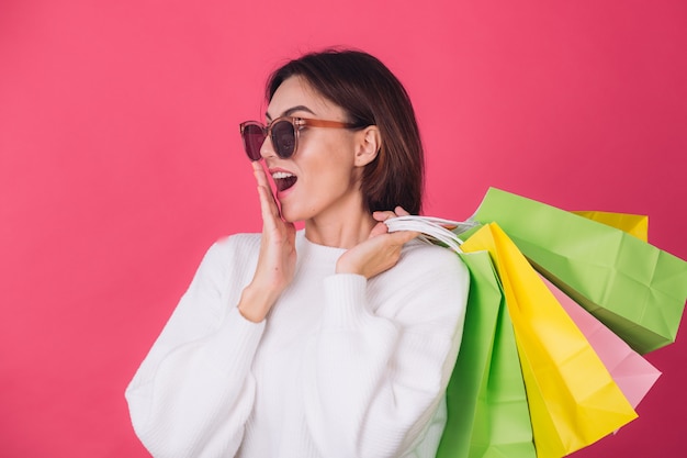 Donna in maglione bianco casual e occhiali da sole sulla parete rossa