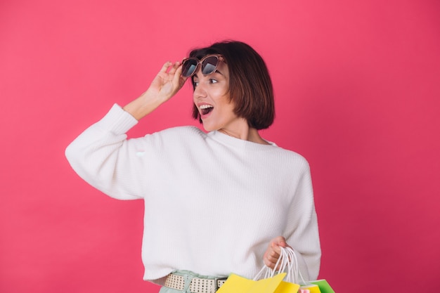 Woman in casual white sweater and sunglasses on red wall