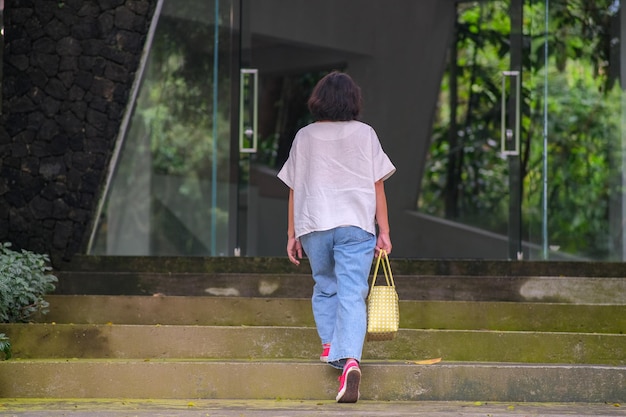 Photo woman casually walking up the steps into glass door entrance under the shade